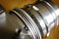 Nahaufnahme eines analogen Kameraobjektivs mit sichtbaren Fokus- und Blendeneinstellringen. Zahlen und Markierungen kennzeichnen die Einstellungen für präzise Fotoanpassungen und fangen den Charme der analogen Fotografie ein.